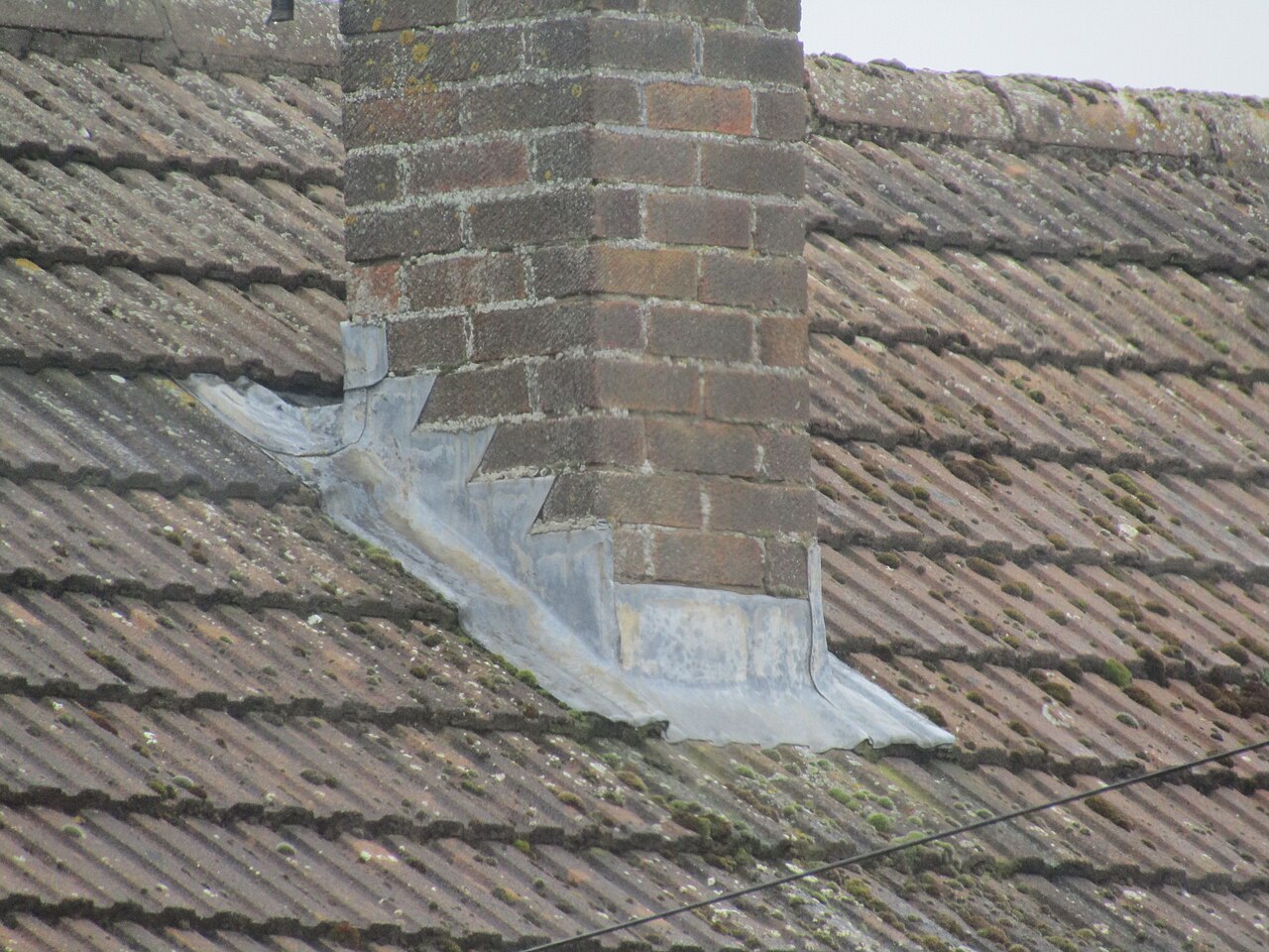 Lead flashing installed around a chimney stack on a residential roof, properly formed lead collar sealed at the chimney base, demonstrating permanent-grade chimney flashing methodology
